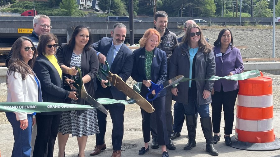 Image: Members of the community hold oversized scissors as part of a ceremony to mark the completio...