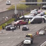 Image: A tow truck removes one of the cars blocking the expressway leading to Seattle-Tacoma International Airport on Monday, April 15, 2024 as people walk by with suitcases toward the airport. A pro-Palestinian protest closed the road to the airport.